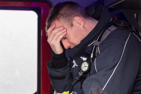A fireman sits with his head in his hands in his fire truck. He appears upset.