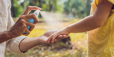 a woman spraying a child's arm with insect repellent